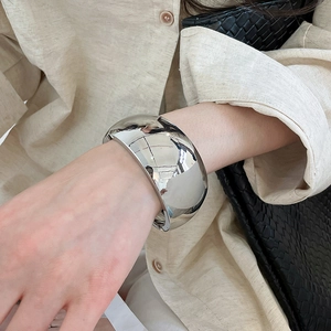 Macro view of a wide silver mirror-finish bangle worn with a linen shirt.