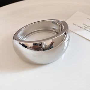 Close-up of a minimalist chunky polished silver wide metal bangle with a spring hinge.