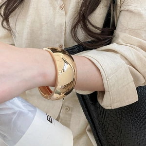 Fashionable glossy gold-toned chunky metal cuff bangle worn on a woman's wrist