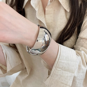 Detailed view of a polished silver metallic wide dome cuff bracelet worn on the wrist