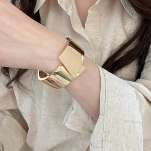 Close-up shot of a bold polished gold metallic cuff bracelet worn on a woman wrist
