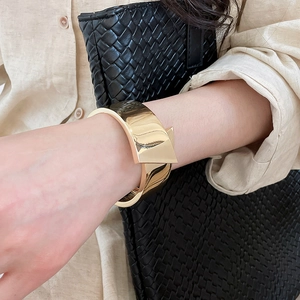 Close-up of a minimalist glossy gold metallic cuff bracelet with geometric fold detail