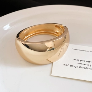 Close-up detail of a polished gold-tone wide dome bangle bracelet on a white plate