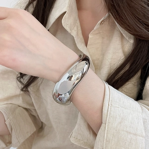 Detailed view of a high-polish silver metal cuff bracelet on a model's wrist