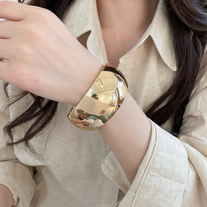 Detailed close-up of a wide polished gold metal cuff bracelet worn on a woman wrist