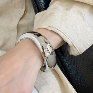 Close-up view of a chunky silver polished metal bangle worn on a wrist with linen shirt