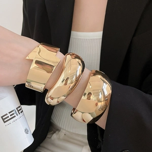 Close-up detail of model wearing three chunky gold polished metallic cuff bracelets set