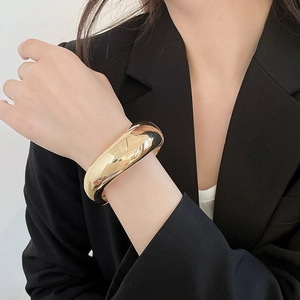 Close-up view of a chunky polished gold-toned metal bangle bracelet worn on the wrist