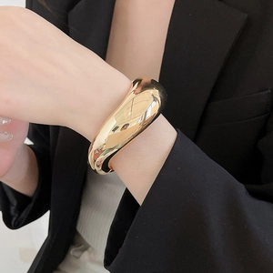 Close-up of a chunky gold-polished metal cuff bracelet on a female wrist.