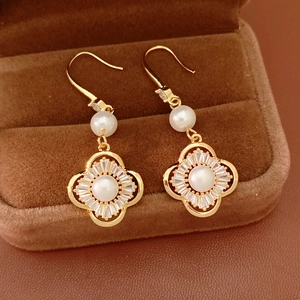 Λεπτομερής προβολή χρυσών σκουλαρικιών τριφύλλι με πέρλες και ζιργκόν σε κουτί
