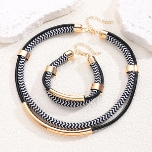 Detail view of a double-layer black and white woven rope jewelry set with gold metal tubes