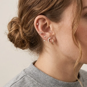 Close-up detail of a curated ear with star, sunburst, and gold hoop zircon earrings.