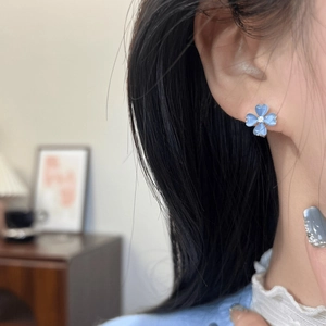 Detailed close-up of icy blue flower stud earrings worn on an ear for summer style.