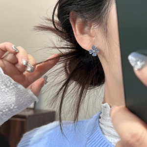 Close-up detail of fresh ice blue flower stud earrings worn on ear with blue sweater