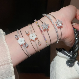 Elegant close-up of stacked zircon and shell flower open bangles worn on the wrist