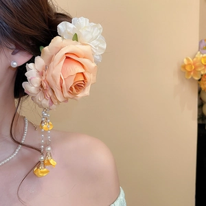 Detail einer eleganten Rosen-Haarklammer mit Perlenanhängern im Haar eines Modells.