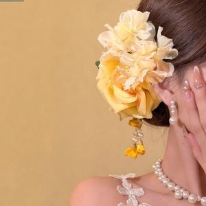 Detailed view of yellow fabric flower hair clip with pearl tassels on a model