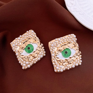 Vista detallada de pendientes cuadrados dorados con diseño de ojo verde y bordes de perlas.