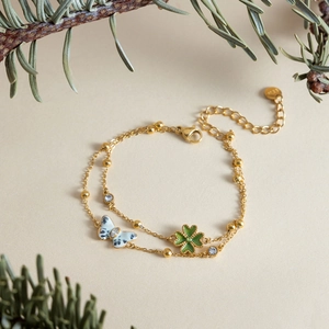 Detail showing elegant gold bracelet with green clover and patterned butterfly charms