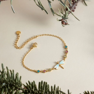 Close-up of golden dragonfly bracelet with colorful zircon stones on pine branch background