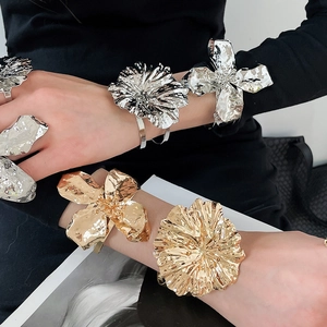 Close-up of gold and silver hammered metal flower bracelets and rings on a model's arms.