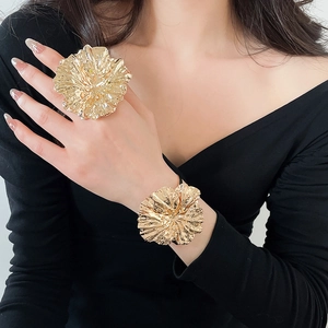 Elegant detail of oversized gold metal flower ring and bracelet set worn on model hand
