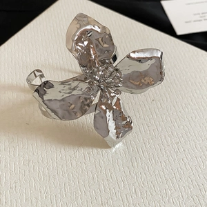 Detailed close-up of an oversized silver flower cuff with a textured, hammered metal finish.