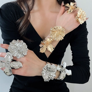 Detailed macro view of oversized metallic flower rings and cuffs in gold and silver.