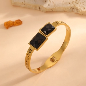 Close-up of gold stainless steel bangle with black square gems and Greek key engraving details