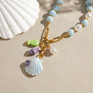 Detailed view of ceramic beach necklace with shell and fish pendants in soft lighting.