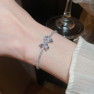 Primer plano de una elegante pulsera de plata con un lazo de circón morado en la muñeca