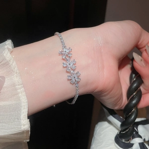 Detalle de una elegante pulsera de oro de 18k con flores de circón en la muñeca.