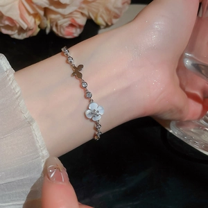 Nahaufnahme eines silbernen Armbands mit feinen Blumen- und Schmetterlingsanhängern.