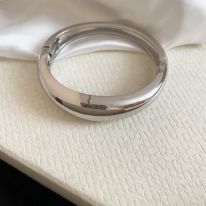 Close-up of a glossy silver geometric irregular metal bangle on a textured background.