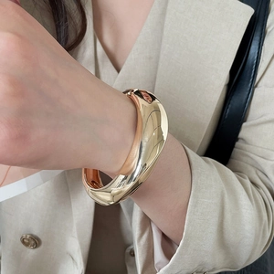 Close-up detail of thick glossy gold irregular geometric metal bangle jewelry on wrist