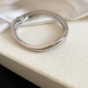 Macro view of a polished silver irregular geometric bangle on elegant white silk background.