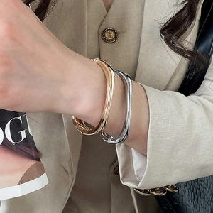 Close-up of gold and silver irregular geometric bangles worn with a beige blazer.