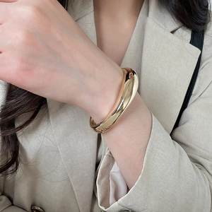 Detailed view of a gold metallic irregular geometric bangle on a model's wrist.