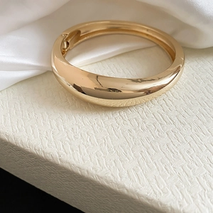 Detailed view of a glossy gold irregular geometric bangle with high-end polished metal finish