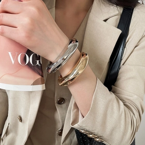 Detail view of chunky irregular gold and silver metal bracelets on a model's wrist