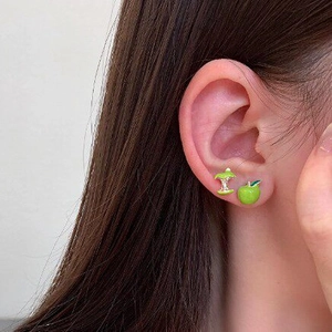 Macro view of cute asymmetrical green apple and apple core stud earrings worn on ear