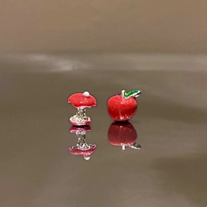 Close-up of asymmetric red apple and bitten apple core enamel stud earrings on a reflective surface