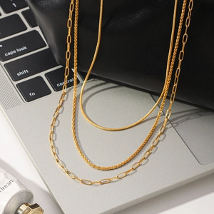 Macro detail of a triple-layer gold-plated stainless steel necklace with paperclip chain.