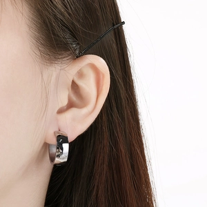 Close-up detail of a minimalist stainless steel polished hoop earring worn on an ear.