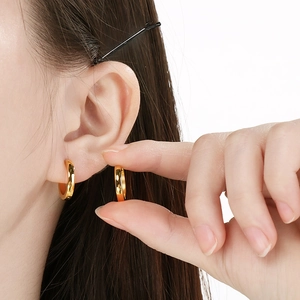Detailed view of minimalist gold stainless steel hoop earrings worn on a model's ear