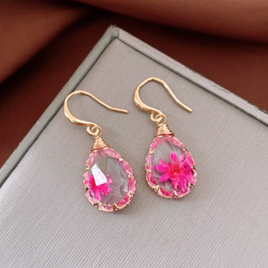 Detail view of handmade waterdrop resin earrings featuring pink dried flowers and gold hooks.