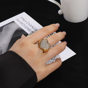 Vista detallada de un anillo ancho de acero dorado con un gran motivo de corazón pavé