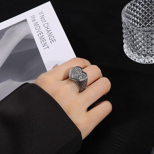 Primer plano de un anillo ancho de corazón de acero inoxidable con pavé de diamantes.