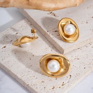 Detalle de pendientes dorados irregulares con perlas sobre piedra con textura