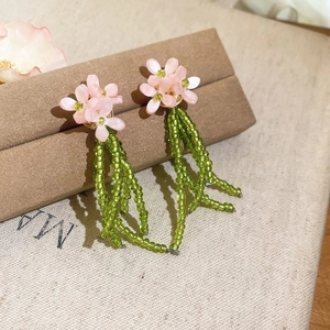 Detailed view of pink flower stud earrings with green beaded tassels in forest style